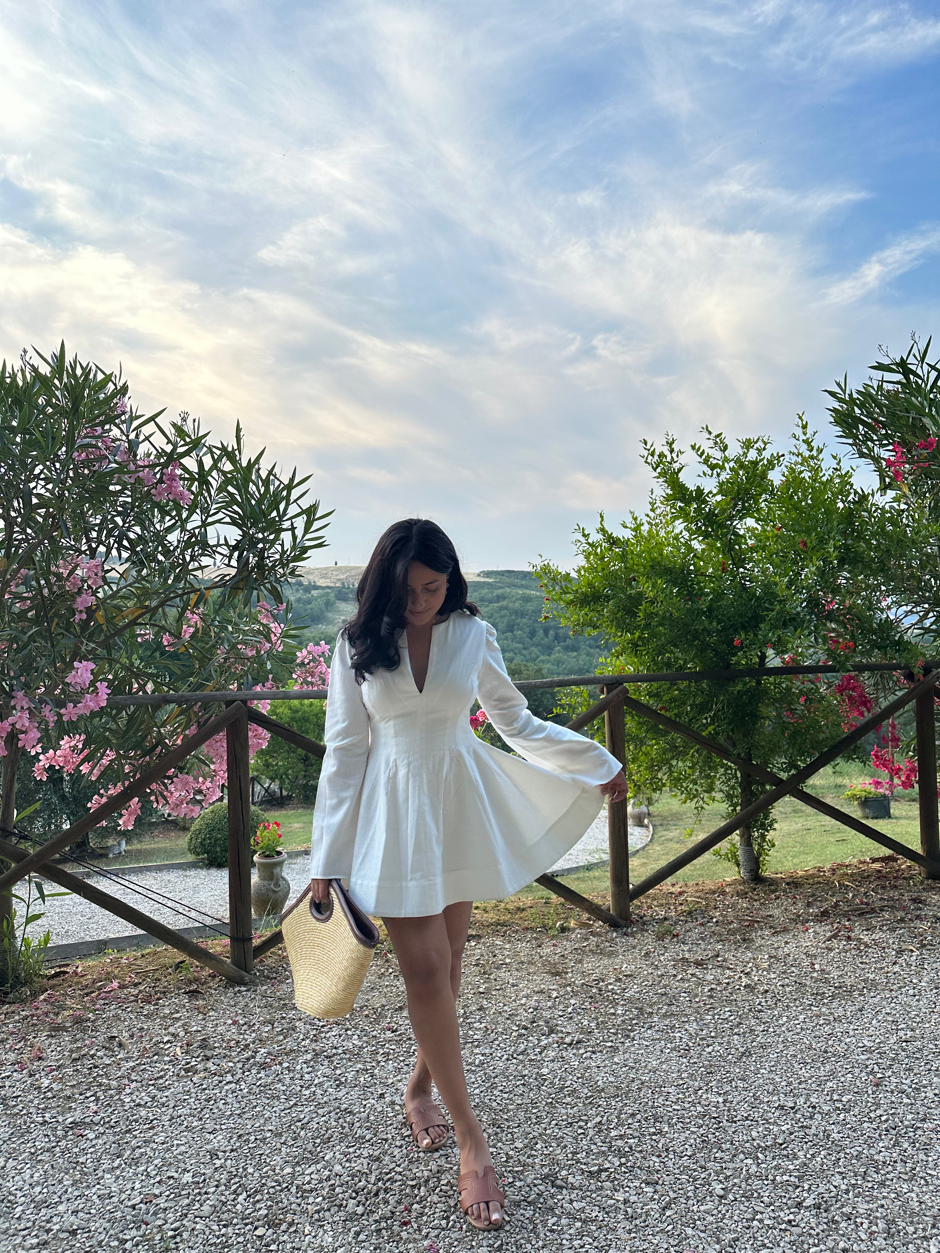 Petite woman who is 5ft in a white mini petite dress standing outdoors with greenery and flowers in the background